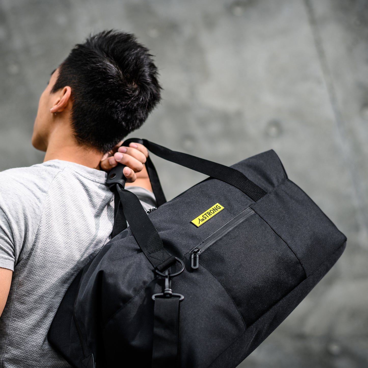man carrying a black sport duffel which has a yellow metallic label