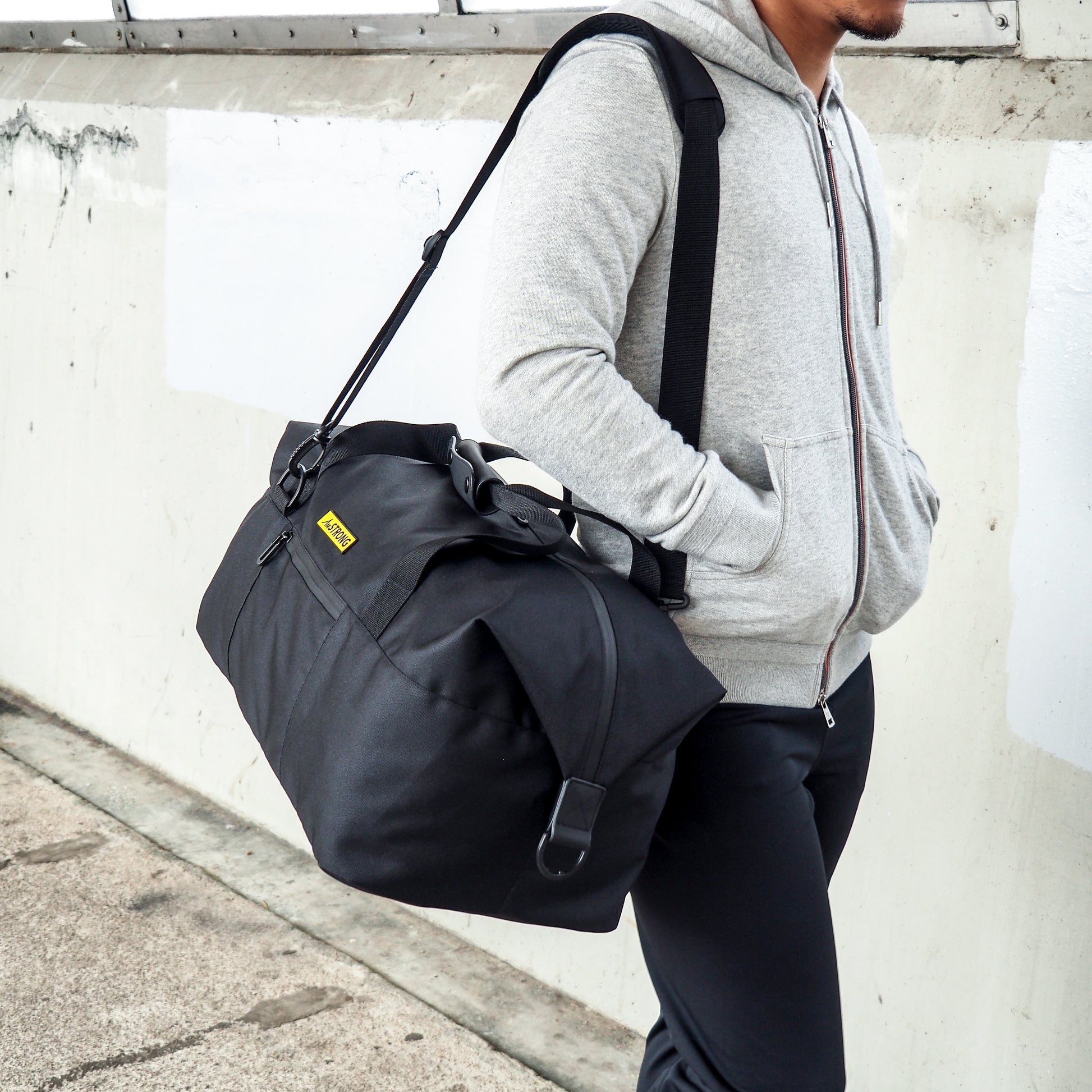 man carrying a black duffel with his hands inside hoodie's pockets