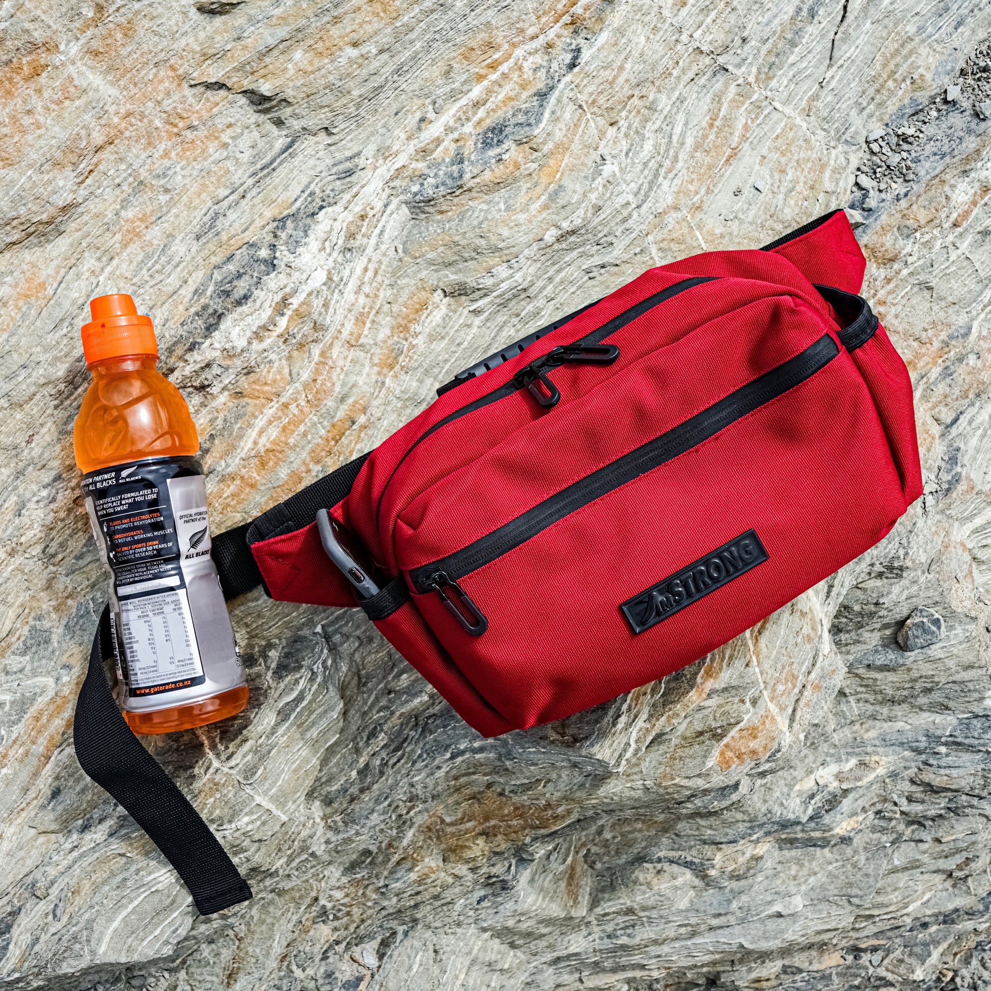 red belt bag and energy drink on a rock