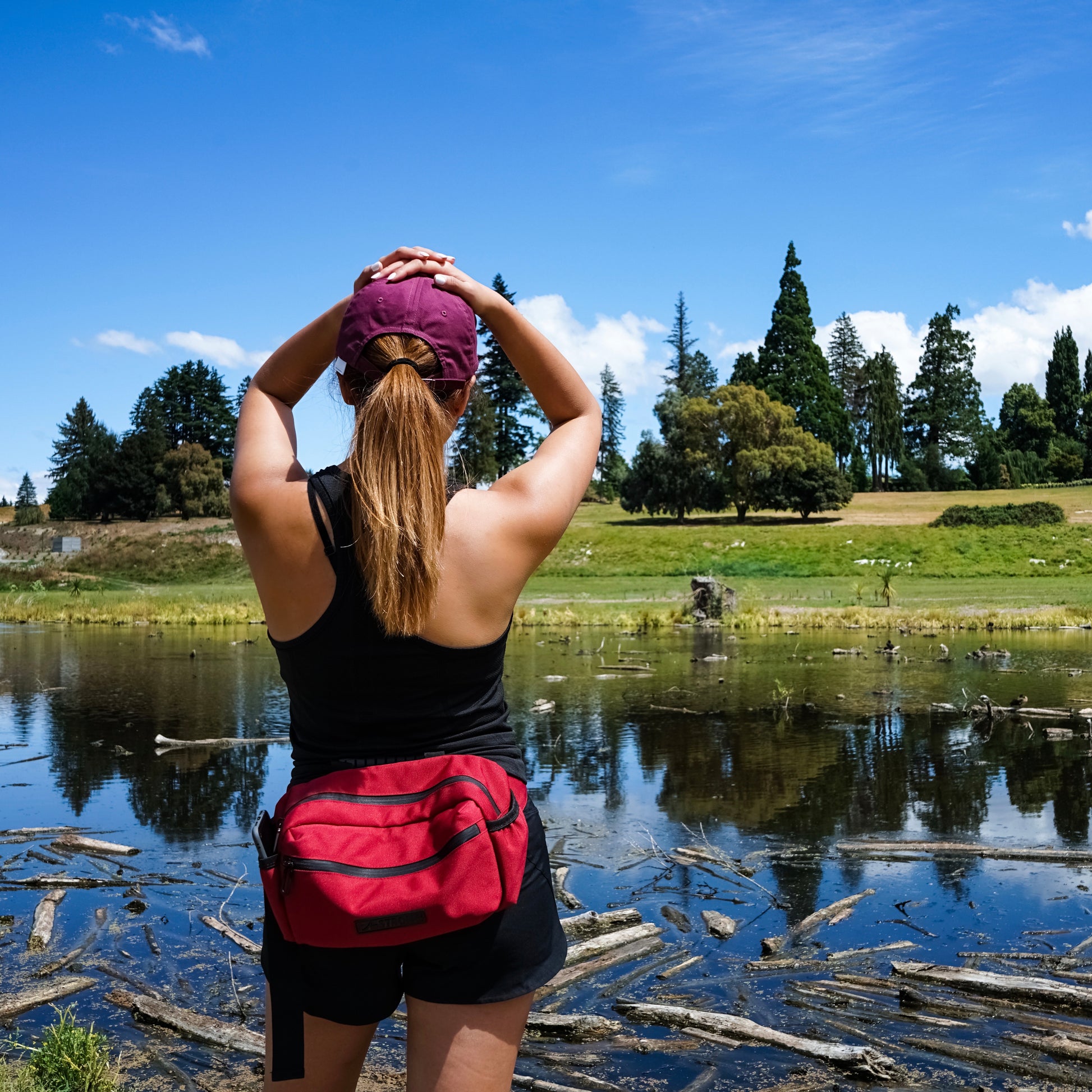woman with a red belt bag in front of a mirror lake